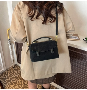 Detail of black crossbody bag with gold hardware and flap closure on a model