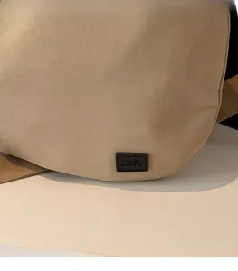 Detail view of khaki crossbody bag with minimalist dark brown rectangular leather logo patch