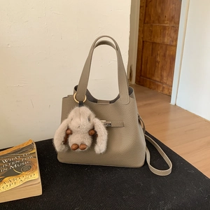 Detail of grey lychee leather bucket bag with metal turn-lock and cute bunny plush charm