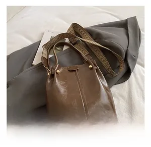 Detail of retro brown bucket bag with wide jacquard strap and gold rivet accents