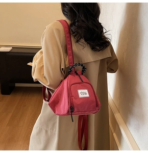 Detail of red checkered canvas backpack with woven handle and brand label on model