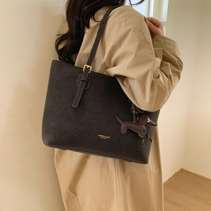 Detail of grey tote bag with adjustable strap and dachshund charm on beige trench coat