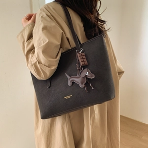 Detail of dark brown leather tote bag featuring a cute dog and chocolate bar charm