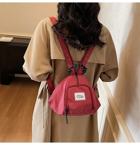 Close-up of red checkered canvas backpack with woven handle on a khaki trench coat