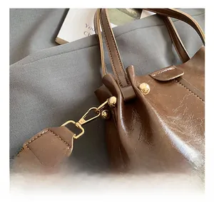 Detail of gold metal hook and woven strap on a brown faux leather bucket bag