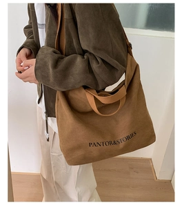 Side view of a brown canvas tote bag with black lettering being worn over the shoulder