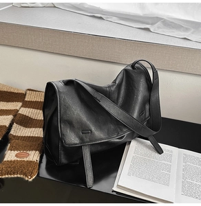 Detailed view of black matte leather messenger bag with large flap and wide strap
