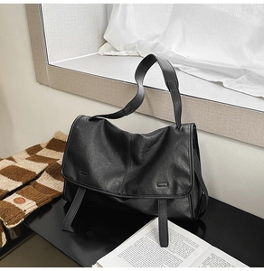 Close-up of black lychee texture leather messenger bag with decorative buckle straps