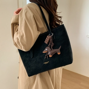 Detail of black suede tote bag with brand logo and cute dachshund charm on beige coat