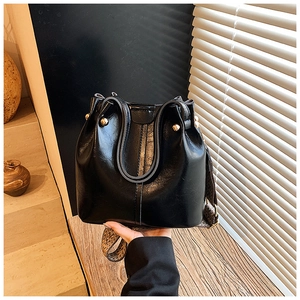 Detail of black glossy bucket bag featuring gold hardware and leopard print wide strap