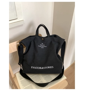 Detail of a black canvas tote bag with white lettering on a wooden chair with books