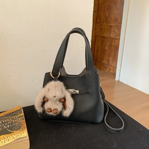 Detail of black lychee grain bucket bag with silver twist lock and plush bunny charm