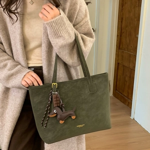 Detail of moss green suede tote bag with brown dachshund charm and brand logo