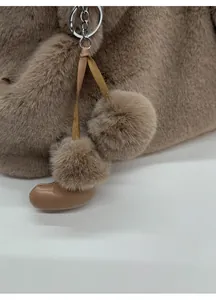 Detailaufnahme der Plüsch-Eimertasche mit braunem Bommel und Mini-Stiefel-Anhänger