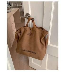 Detail of dark brown canvas tote bag with black print hanging on a white wooden door