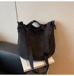Detail of a black canvas crossbody bag showing pockets, drawstring and adjustable strap