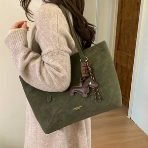 Detail of dark green tote bag featuring a sausage dog charm and gold logo branding