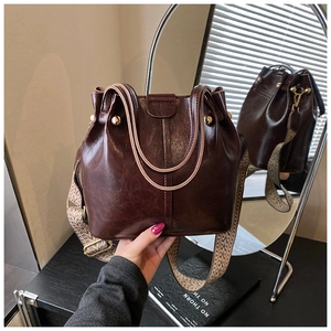 Detail of dark brown bucket bag with shiny finish, golden rivets and wide patterned strap