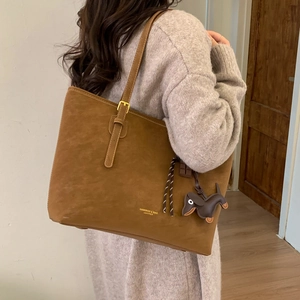 Detail of dark brown leather tote bag with shoulder strap and a cute dog charm accessory