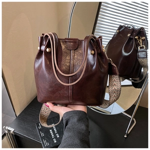 Detail of dark brown vintage leather bucket bag with wide woven strap and metal rivets