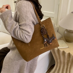 Detail of caramel suede tote bag with brand logo, contrast stitching, and puppy charm