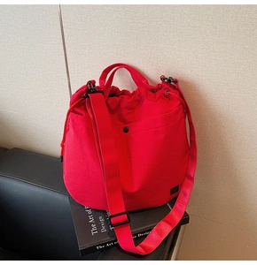 Detail of red drawstring nylon bucket bag with adjustable wide strap and black logo patch