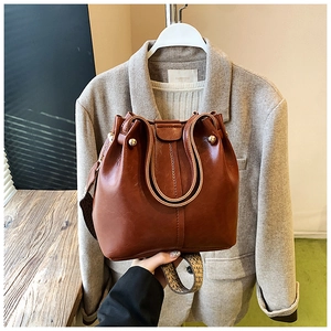 Detail of caramel brown bucket bag with vintage leather texture and woven shoulder strap