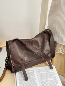 Retro dark brown crossbody bag with wide strap on a minimalist wooden desk setup