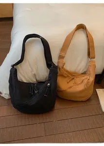Detail view of canvas crossbody bags in black and camel colors with fringe zip pullers