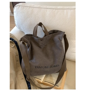 Detail of coffee canvas tote bag featuring printed lettering and adjustable strap on a sofa