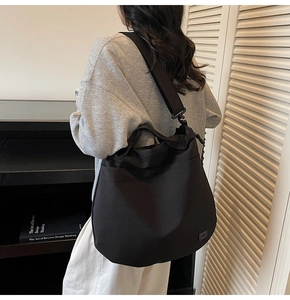 Side view of large black nylon crossbody bag featuring drawstring details and wide strap