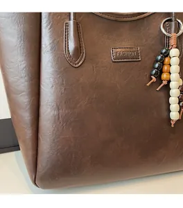 Detail of vintage brown leather tote bag with FASHION logo and wooden bead charm