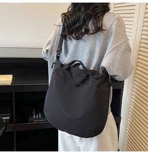 Model wearing a black wrinkled nylon tote bag with adjustable strap in a modern room