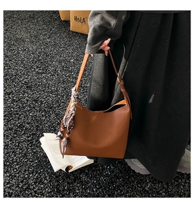Dettaglio di una borsa a secchiello marrone testurizzata con elegante foulard in seta a pois