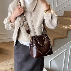 Detail of dark brown bucket bag featuring glossy finish and vintage woven shoulder strap