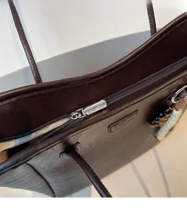 Detail of silver zipper closure and beaded pendant on dark brown leather tote bag