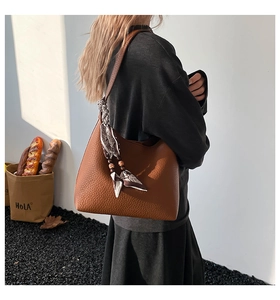 Dettaglio borsa a secchiello in pelle marrone con foulard in seta e perle di legno