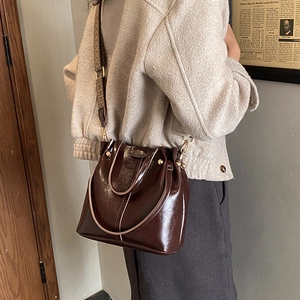 Detail of dark brown glossy bucket bag with wide woven strap and gold hardware