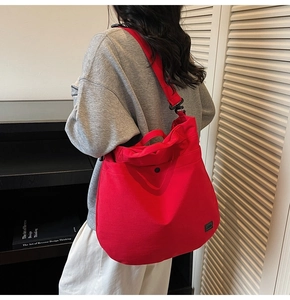Rear view of a large red canvas crossbody bag with wide black strap and magnetic button