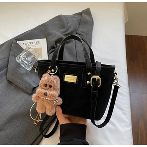 Detail of black matte bucket bag with golden chain handle and plush bear charm decoration