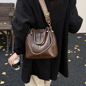 Close-up of retro brown glossy bucket bag with a wide patterned strap and gold hardware