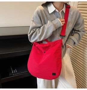 Detail of red canvas crossbody bag showing pockets, metal snaps, and wide strap