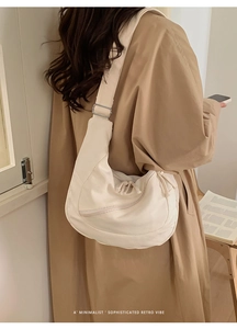 Minimalist beige half-moon canvas crossbody bag worn over a trench coat for daily use