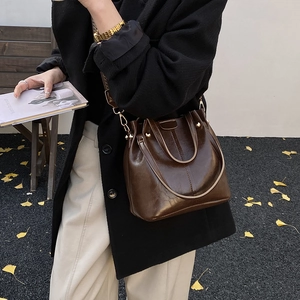 Detail of dark brown glossy leather bucket bag with wide strap on elegant model