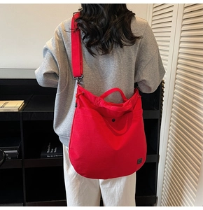 Rear view of a model wearing a large red canvas crossbody bag with adjustable strap