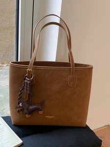 Brown suede tote bag with dachshund charm and gold logo on high-quality minimalist background