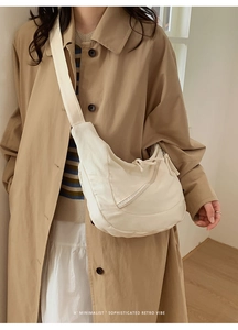 Détail d'un sac demi-lune en toile beige avec bandoulière large et design minimaliste