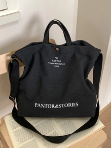 Black canvas tote bag with white lettering and long shoulder strap on a wooden chair