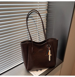 Détail du sac cabas marron foncé avec étiquette FASHION et pompon perlé tricolore