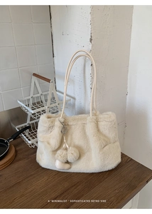 Nahaufnahme der cremefarbenen Kunstfell-Tasche mit weicher Textur und Bommel-Anhängern